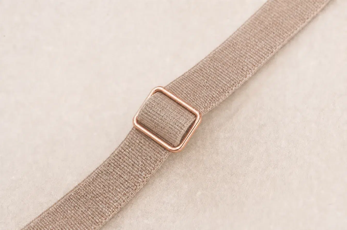 Rose-gold tri-glide correctly threads a folded beige lingerie strap for secure adjustment